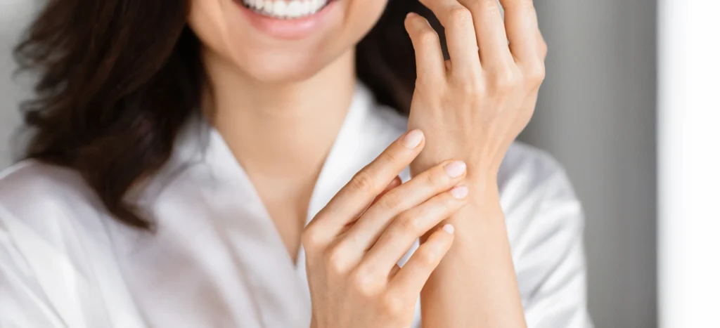 A woman in a white bathrobe applying Sarna Calm + Cool Anti-Itch Lotion on her wrists
